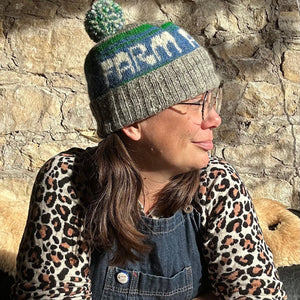 Person wearing a knitted hat with 'Farm' on it against a stone wall.