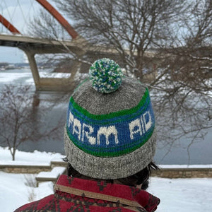 Person wearing a knitted hat with a pom-pom in a snowy landscape with a bridge in the background